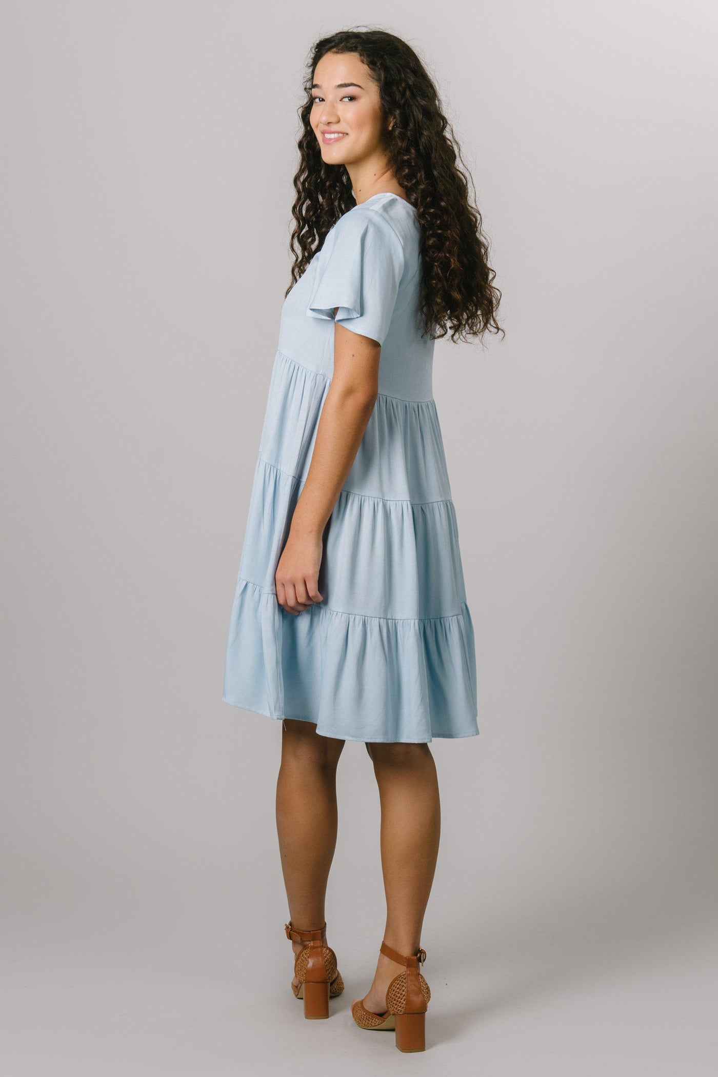 A back shot of a modest, loose fitting everyday dress that features a scoop neck and flutter sleeves in baby blue.