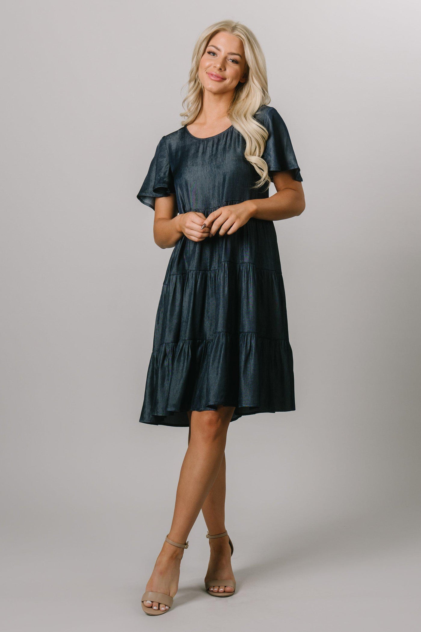 Front shot of a dark denim knee length dress, the model is wearing a size small. This is a swing dress with tiers and flutter sleeves. Modest Dresses - Modest Clothing - Everyday Modest Dresses - Bridesmaid Modest Dresses