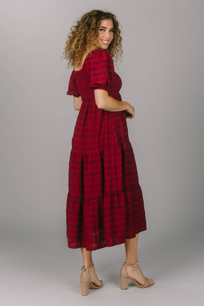 Modest everyday dress featuring a tiered, midi length skirt. This red dress has a square neckline and puffed sleeves. This perfect modest dress has a horizontal striped pattern.