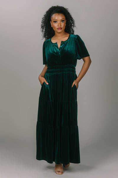 Front view of modest everyday and bridesmaid emerald colored dress. This dress is velvet, has a v-neckline, and a tiered skirt. This modest dress for women is floor length and super comfortable.