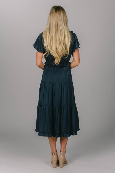 Back view of a navy modest bridesmaid dress. It has a v-neckline and flutter sleeves. Its draping and tiered skirt make for the perfect modest bridesmaid dress.