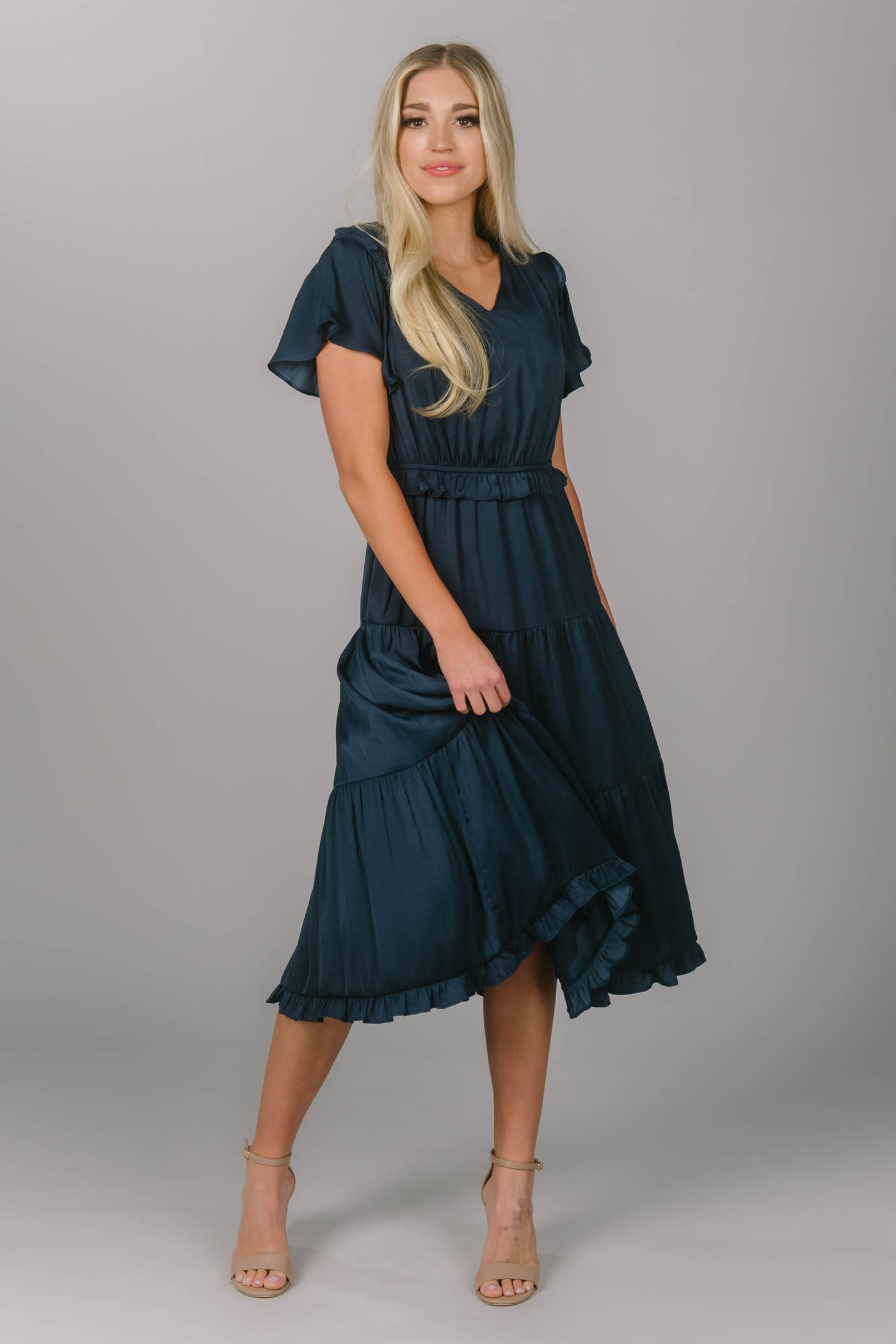 Front view of a navy modest bridesmaid dress. It has a v-neckline and flutter sleeves. Its draping and tiered skirt make for the perfect modest bridesmaid dress. 
