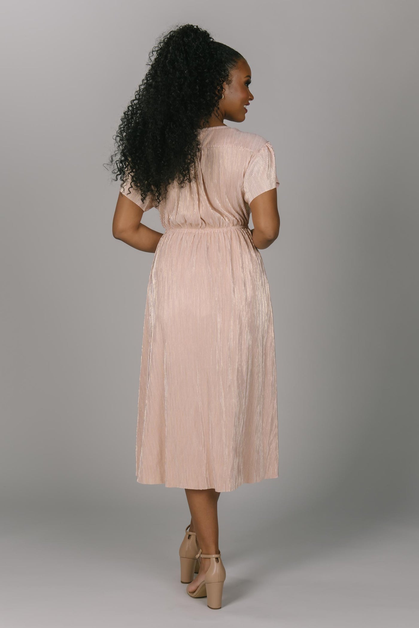 Back view of metallic modest bridesmaid dress. This dress hits mid-calf and is a v-neckline. The sleeves are flutter sleeve style. This pink/gold color makes the perfect bridesmaid dress.