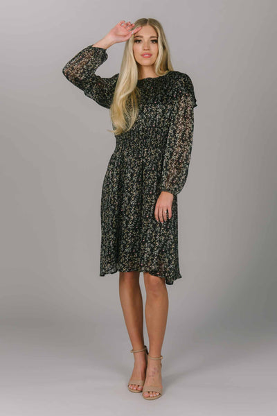 Front view of black modest dress with leaf -like pattern. It has beautiful bishop sleeves and a high scoop neckline.  It is knee length. and quite the perfect modest holiday dress and/or everyday dress. 