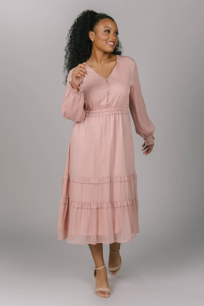 Front view of pink modest dress with long sleeves. It is tiered with buttons down the top of the dress. The modest bridesmaid would fall in love with this dress. 