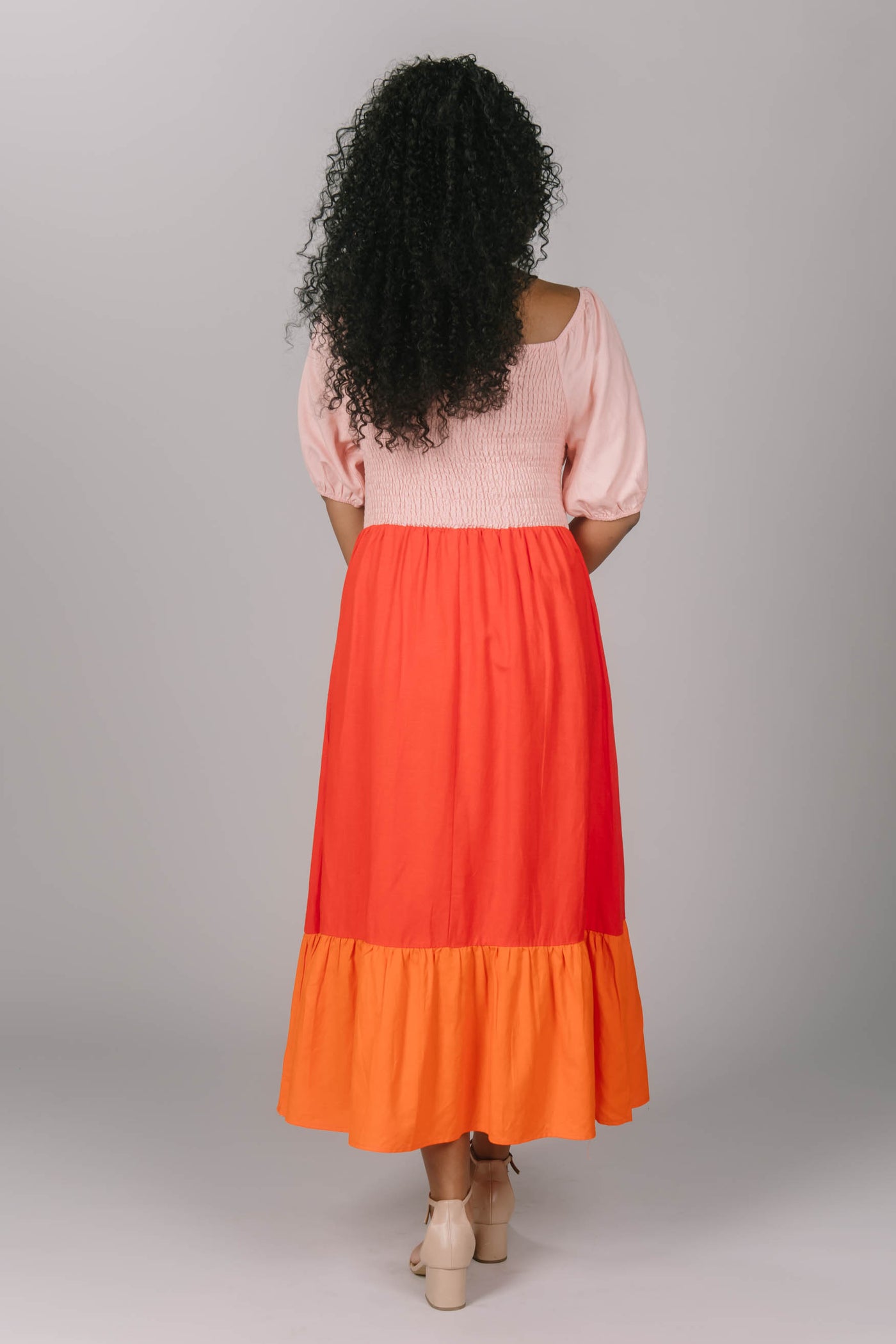 Back view of the smocked color block midi dress. This modest everyday dress has a square neckline and a tiered skirt. It is pink, red and orange bringing more love and color to any modest woman.