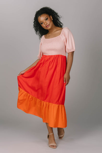Front view of the smocked color block midi dress. This modest everyday dress has a square neckline and a tiered skirt. It is pink, red and orange bringing more love and color to any modest woman.