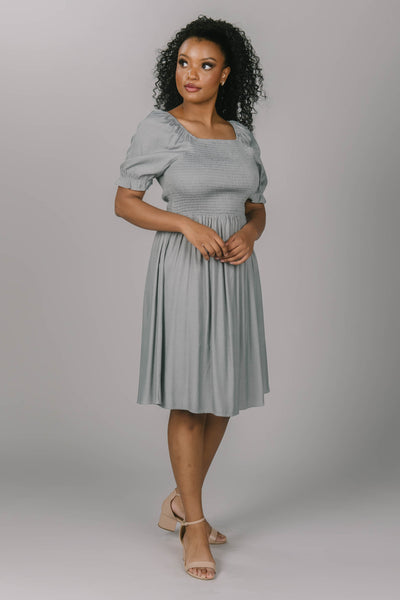 Front view of the smocked puff sleeve dress. It has a beautiful drizzle gray color. This modest dress has a square neckline and is knee length.